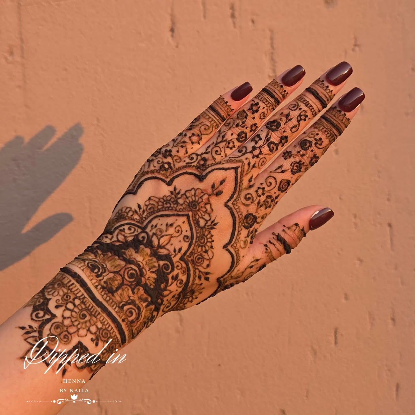 Dense floral henna on the back of the hand against a warm wall