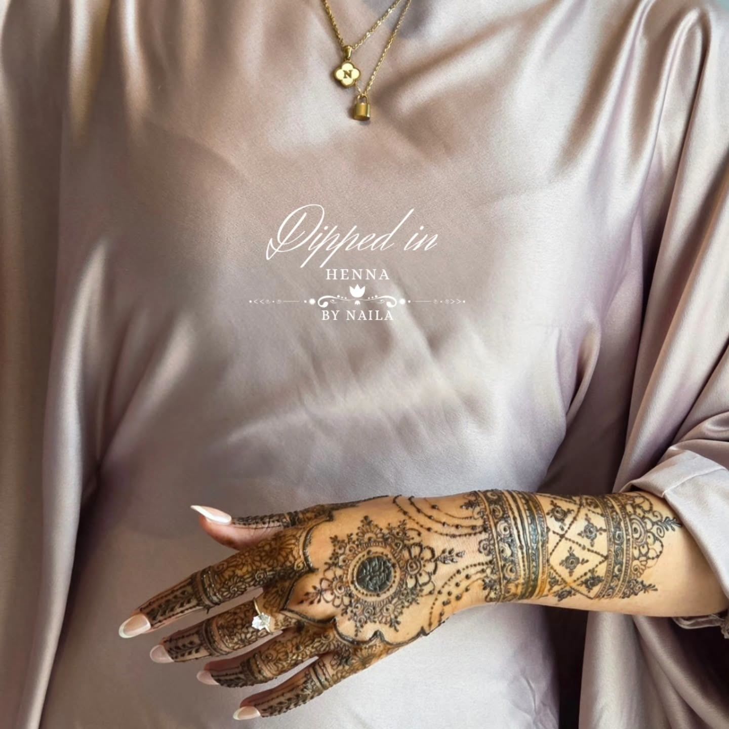 Hand with a detailed henna design resting against a satin Eid outfit and gold necklace