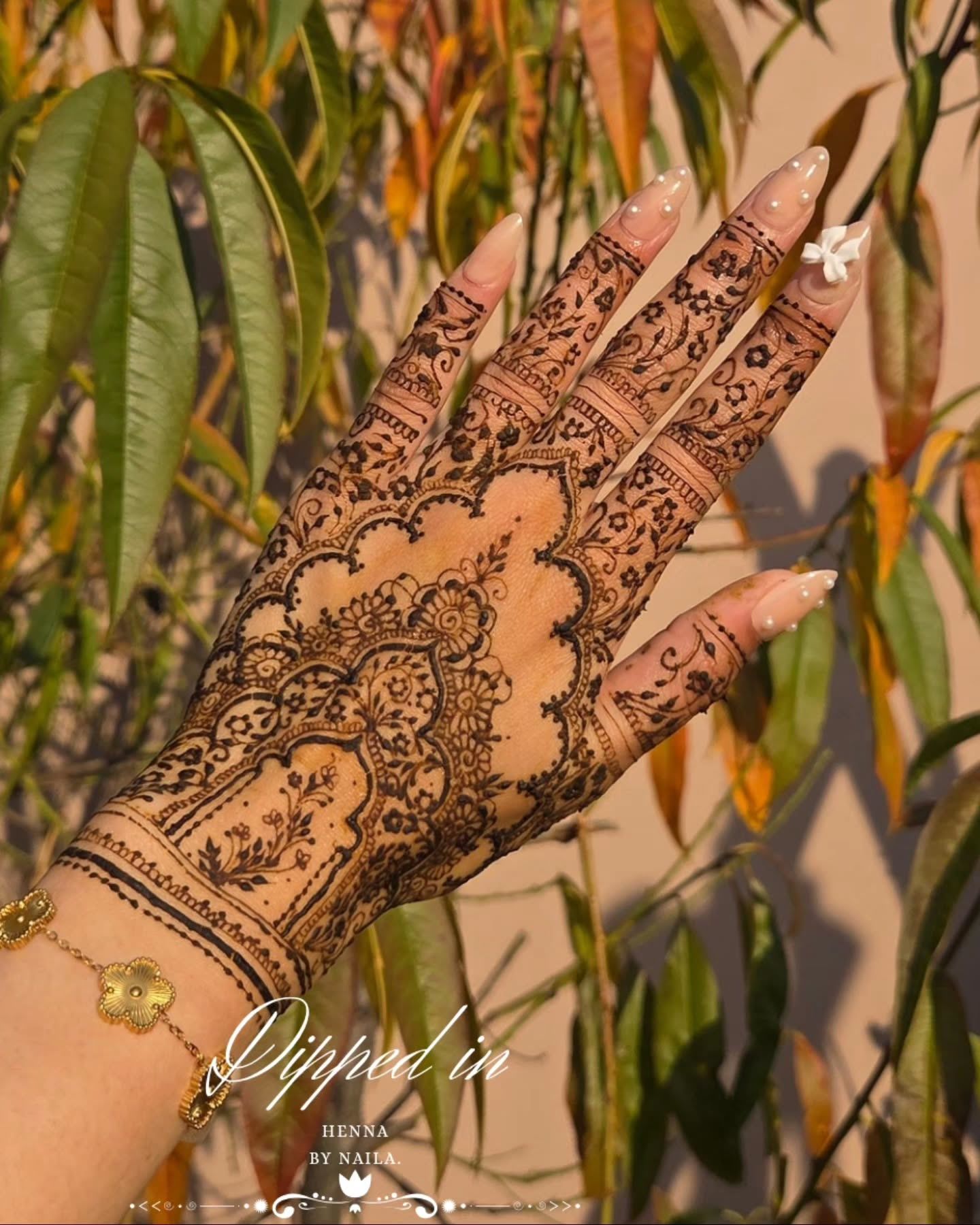 Lace-like henna on the fingers against a warm wall and leaves